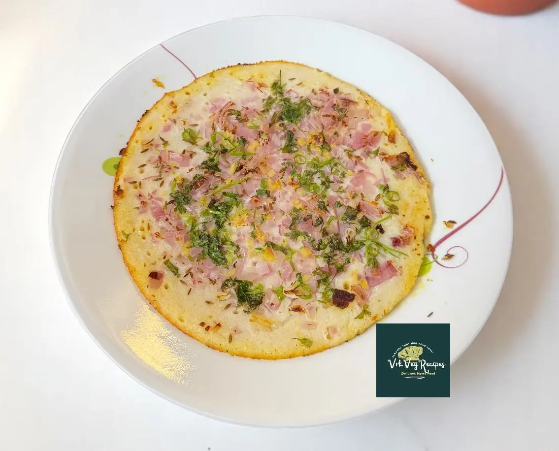 Easy South Indian Onion Uttapam Recipe Onion uttapam topped with onions, chillies, and herbs served hot with coconut chutney on a ceramic plate.