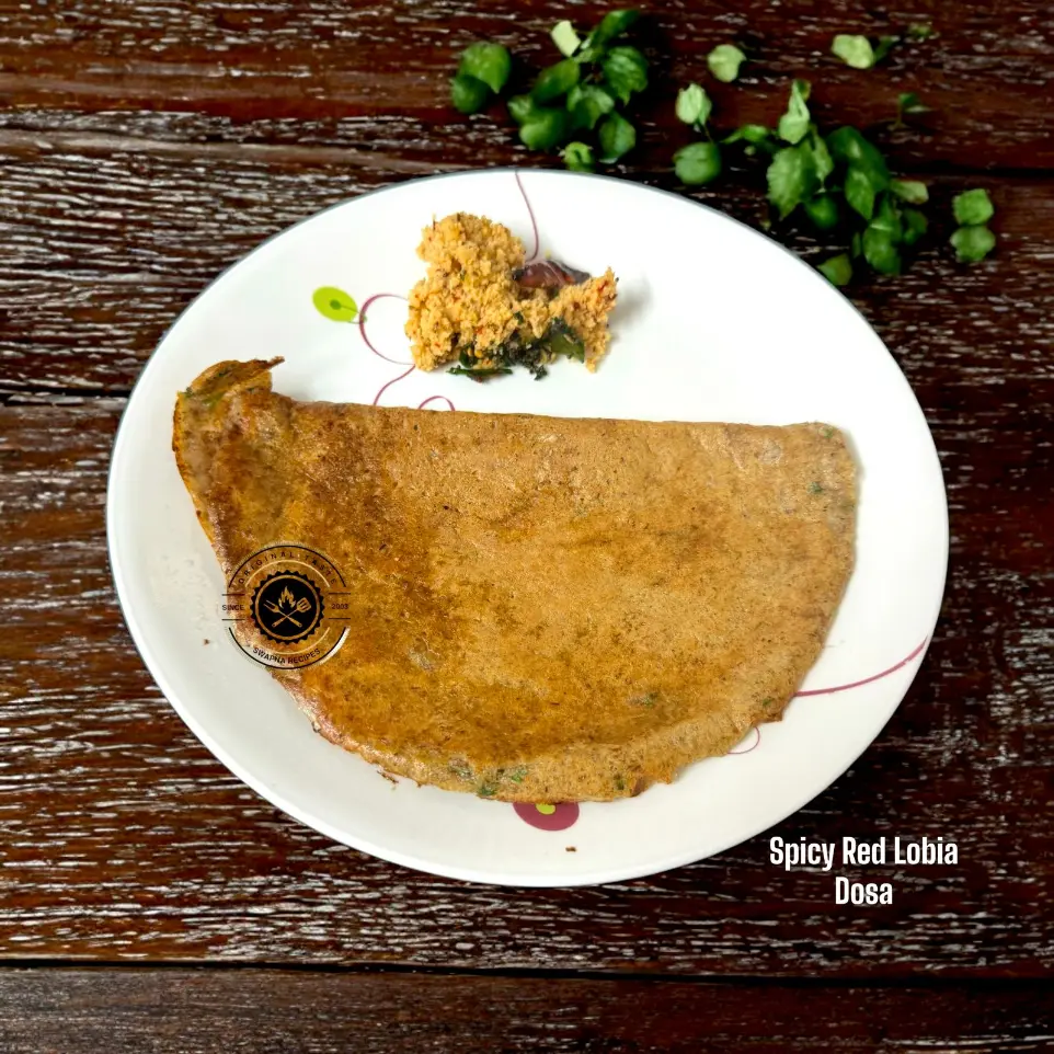 Spicy red cowpea dosa loaded with pepper, green chillies, and herbs, sizzling hot on a dosa pan.