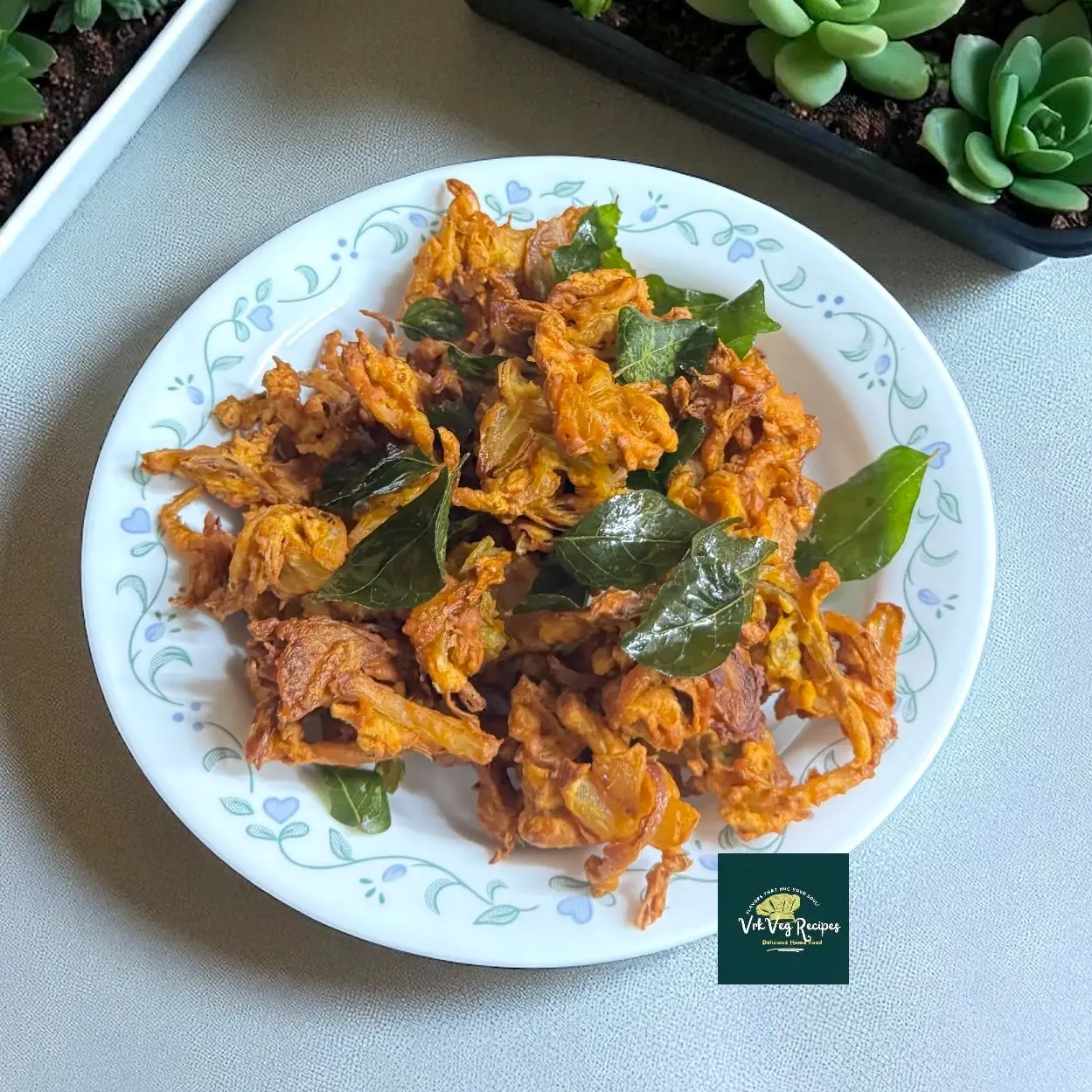 Crispy Onion Pakodi—golden, craggy fritters of onion in besan and rice flour, flecked with green chilli, topped with fried curry leaves; perfect with hot tea.