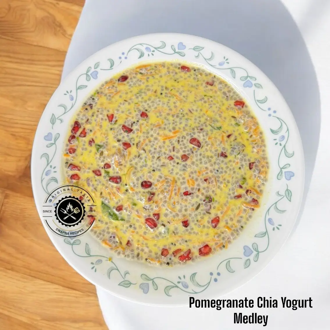 Close-up of pomegranate seeds popping against creamy chia yogurt with grated carrot, green chillies, curry leaves and golden-fried cashews—vibrant and textured.