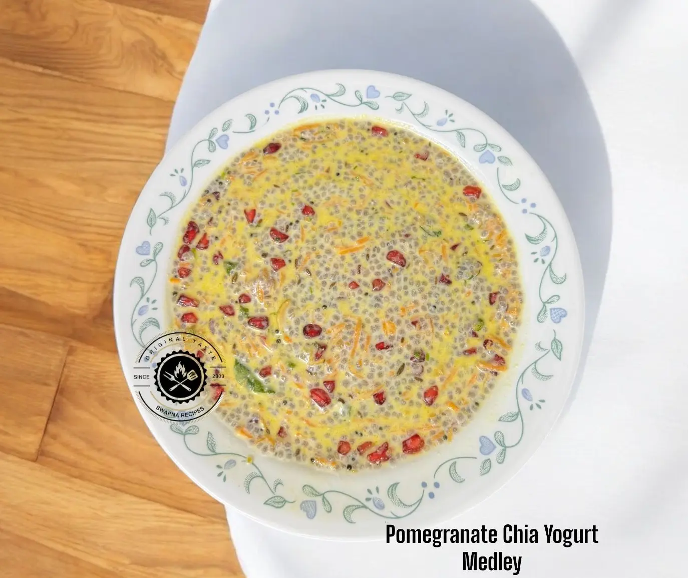 A colorful bowl of Pomegranate Chia Yogurt Medley with soaked chia, curd, grated carrot, chopped green chillies, roasted cashews and coriander—served chilled.