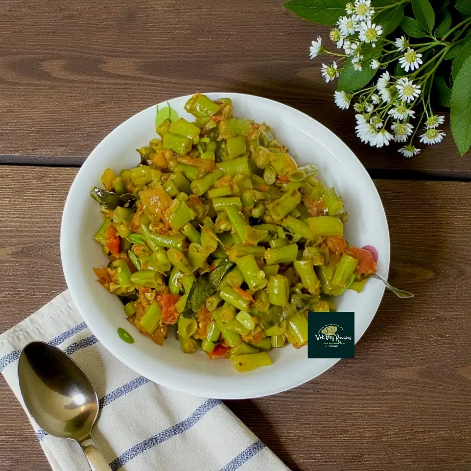 Top-down view of a rustic bowl of long beans masala with vibrant tomatoes and onions, showing textured spices, cumin seeds and a sprinkle of chopped coriander.
